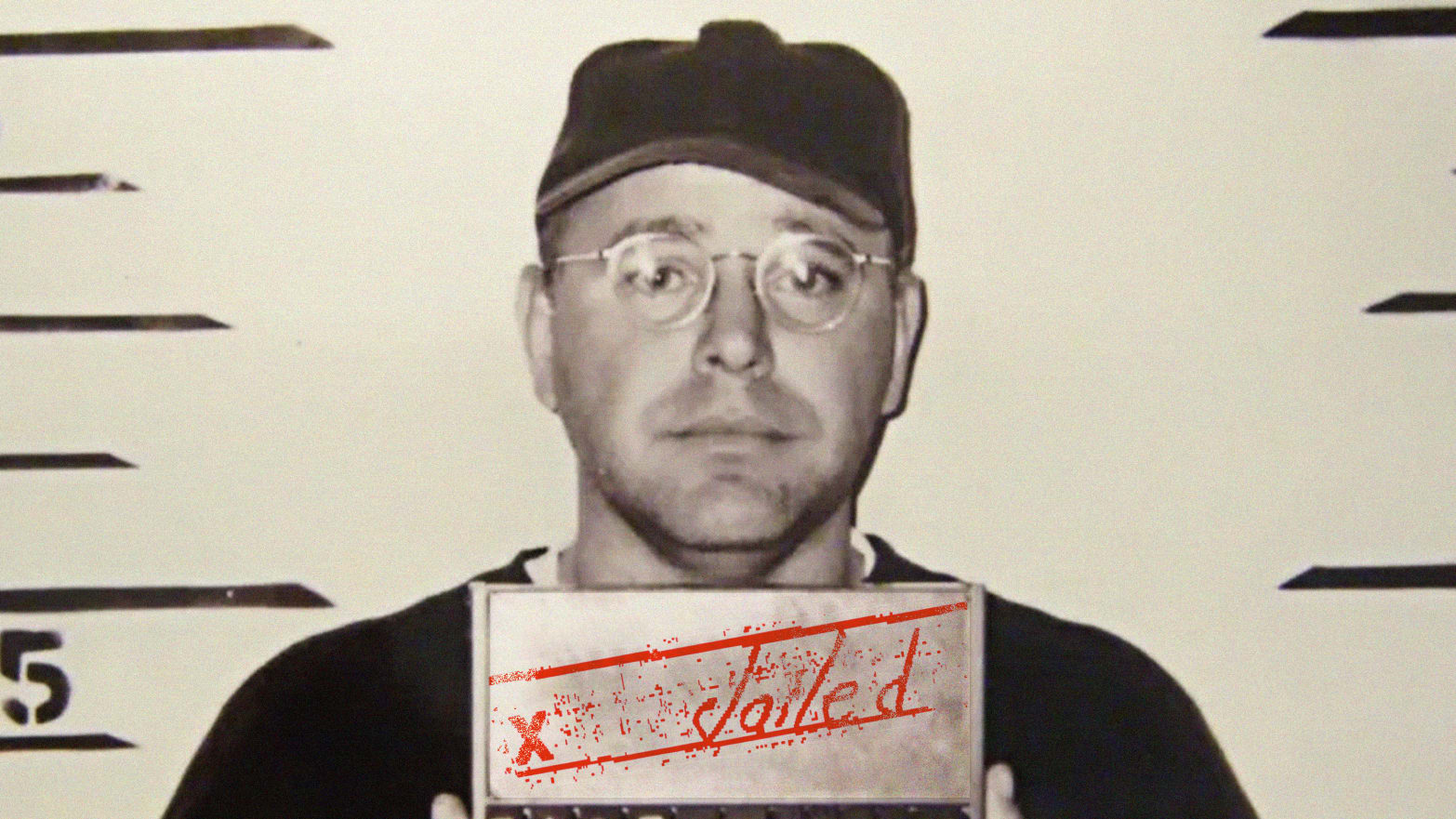 Tim Walz in a mugshot wearing a baseball cap and glasses