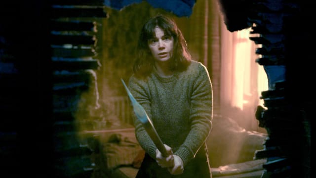 Ruth Wilson holds an axe and peers through a hole in the wall in a still from ‘The Woman in the Wall’