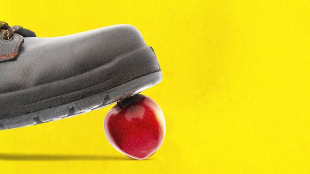 A photo illustration of a boot stepping on an apple on a yellow background