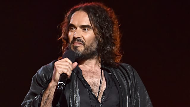 Russell Brand speaks into a microphone at the MusiCares Person of the Year ceremony.