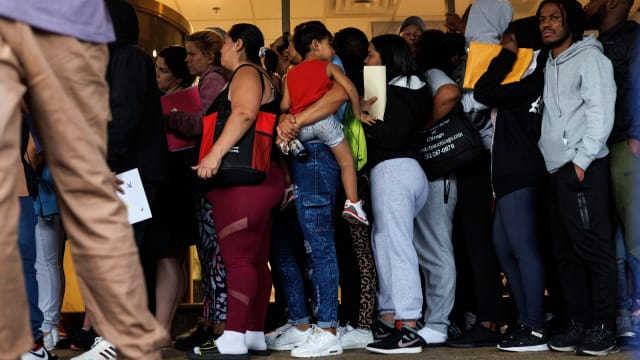 A group of migrants and members of the public wait in line outside an Illinois Department of Human Services office.