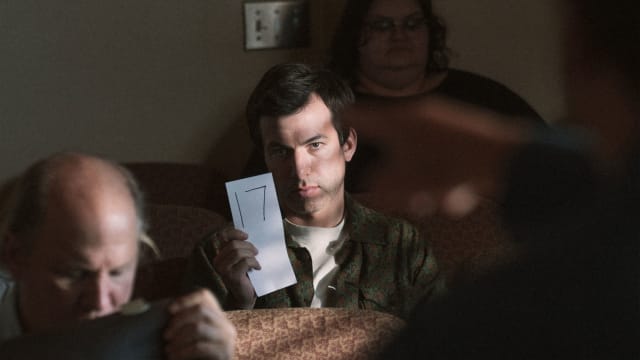 Nathan Fielder holds up a card with a number in it in a still from 'The Curse'