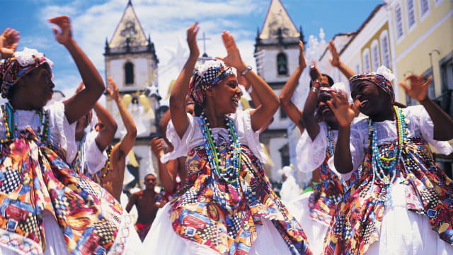 Black women clap and dance in the streets of Salvador, Brazil.