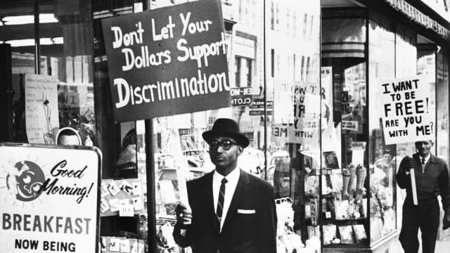 A photo including a Picketer demanding an end to lunch counter segregation made their first appearance outside a Woolworth store in Lynchburg, Virginia.