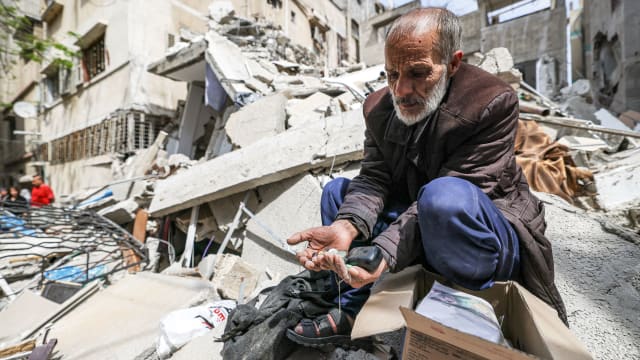 A Palestinian man holds coins in the rubble in Gaza City