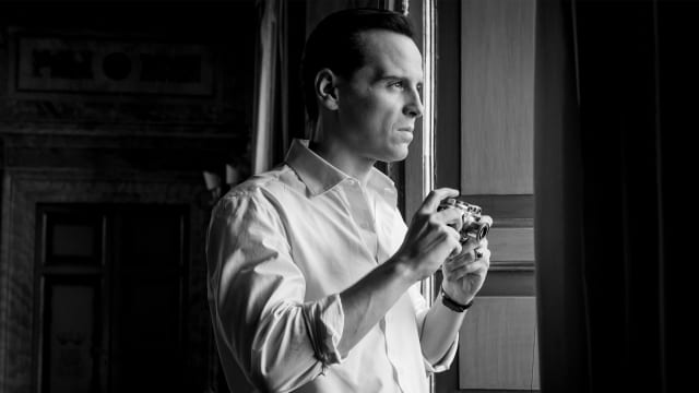 Andrew Scott holds a camera in a window in a still from 'Ripley'