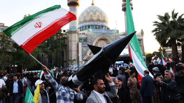 A photo including Iranians carrying a model of a missile 