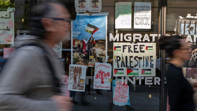 A woman passes by a wall of pro-Palestine signs and posters displayed on windows of The New School.