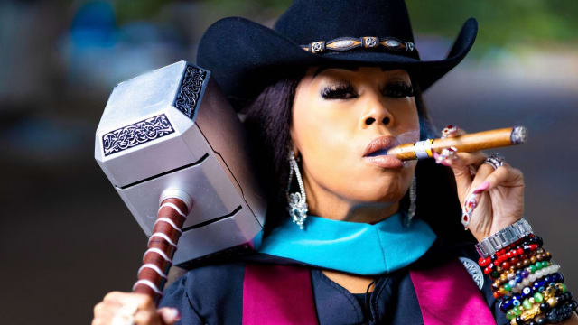A close up portrat of Candice Matthews smoking a cigar and holding a Viking hammer