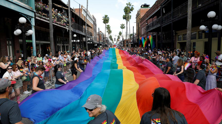 A massive pride flag is carried through a Tampa street during a parade.