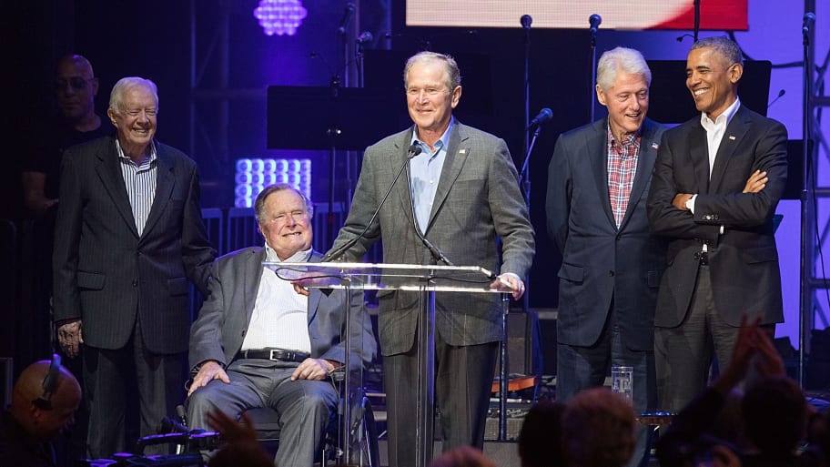 Former presidents Jimmy Carter, George H.W. Bush, George W. Bush, Bill Clinton and Barack Obama stand in front of a podium.