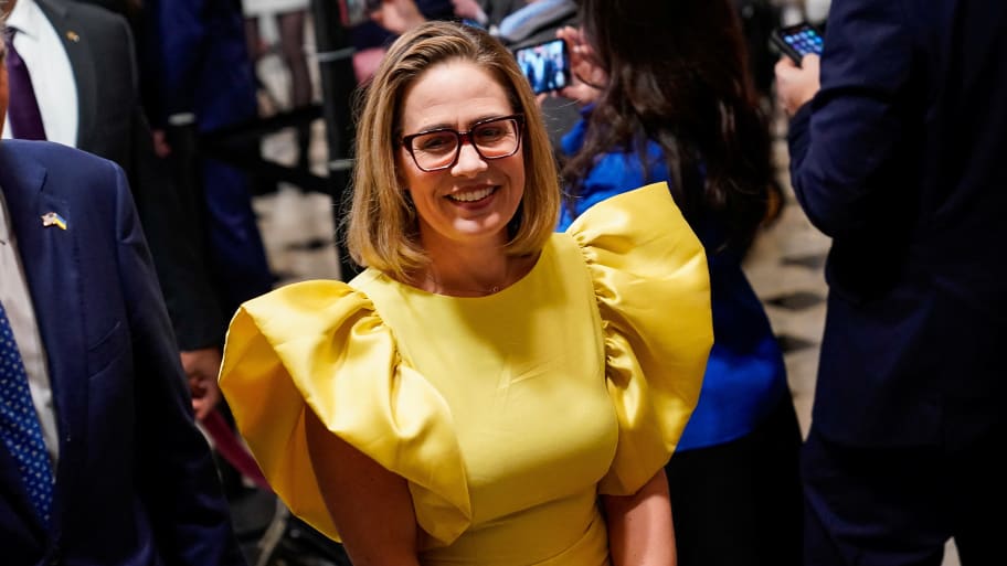 Kyrsten Sinema smiles in a bright yellow dress.