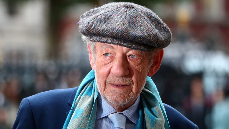 Ian McKellen stares forward while wearing a hat and scarf outside.