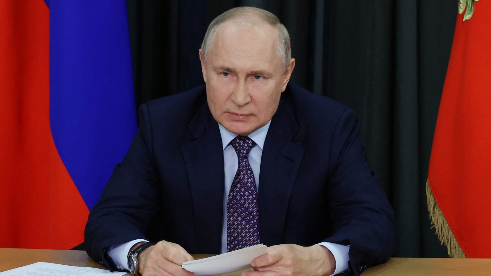 Russian President Vladimir Putin leans on desk at a meeting.