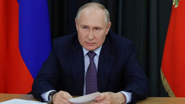 Russian President Vladimir Putin leans on desk at a meeting.