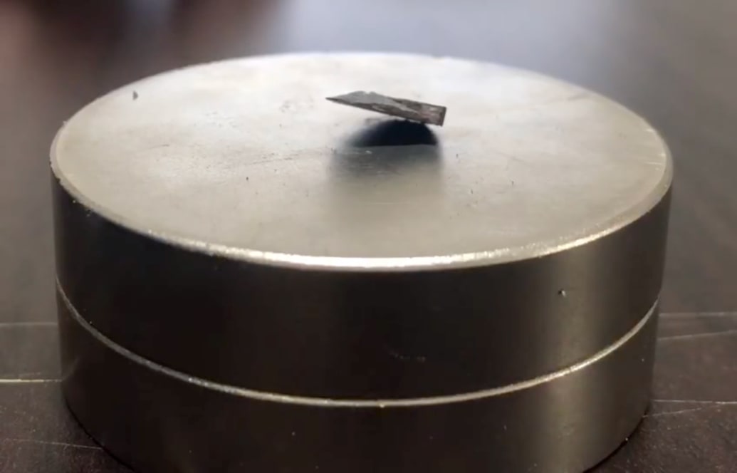 A dark grey material floats above a light grey magnet. 