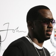 Sean Combs smiles in front of a logo for his fashion brand, Sean John.