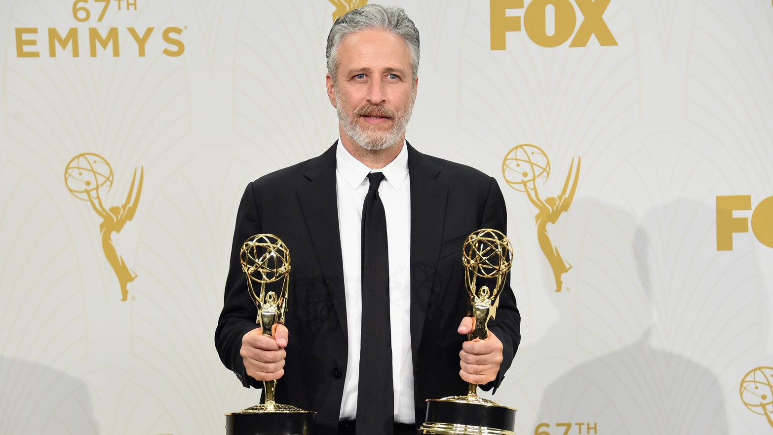 A picture of Jon Stewart holding two Emmys.