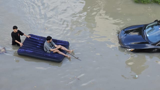 wo men use an inflatable bed to float above the water as downpour causes heavy flooding in Dubai