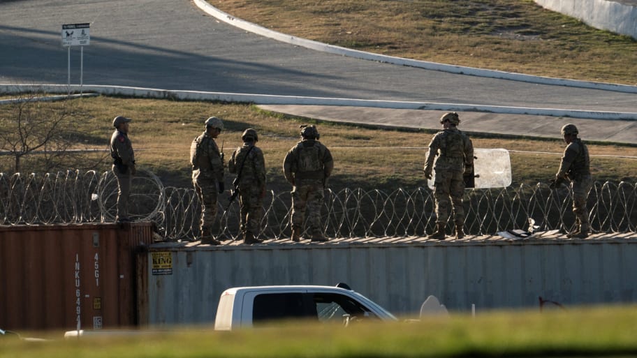 U.S. National Guard soldiers stand on shipping containers which are used as border fences on the bank of the Rio Grande river in Eagle Pass, Texas.