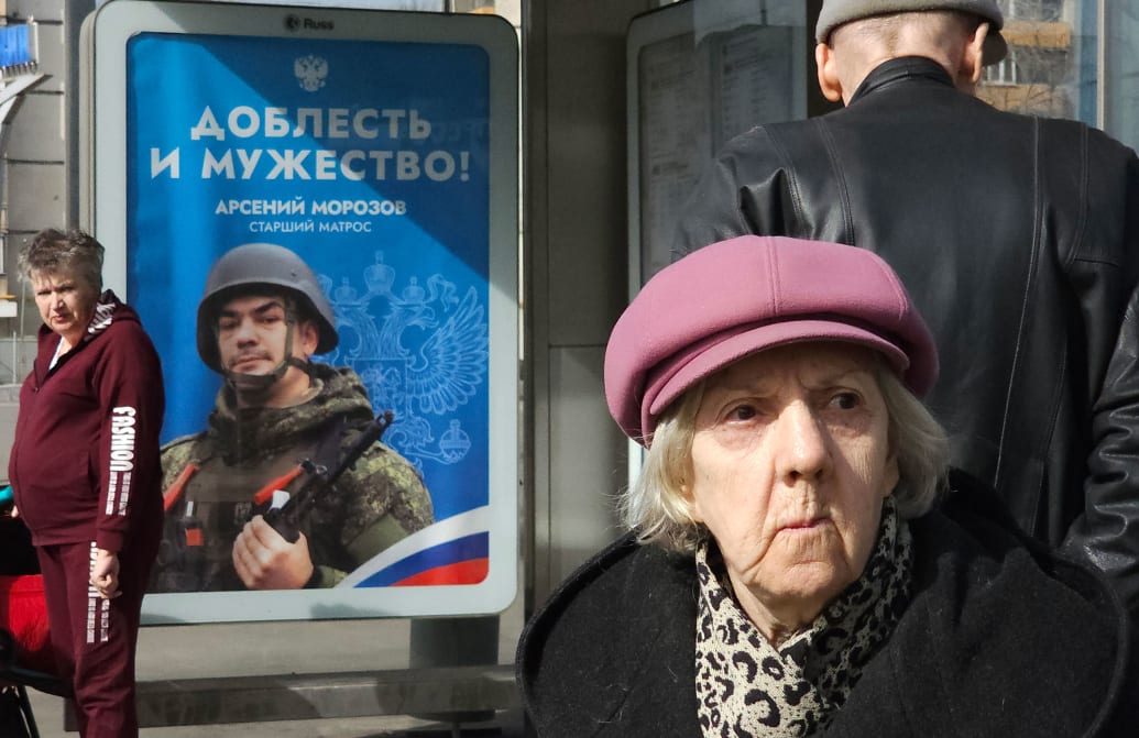 A photo of a woman next to a Russian propaganda poster