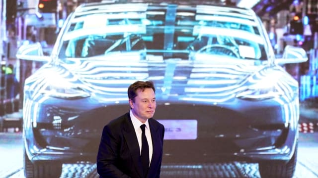 Elon Musk in front of a picture of a Tesla Model 3