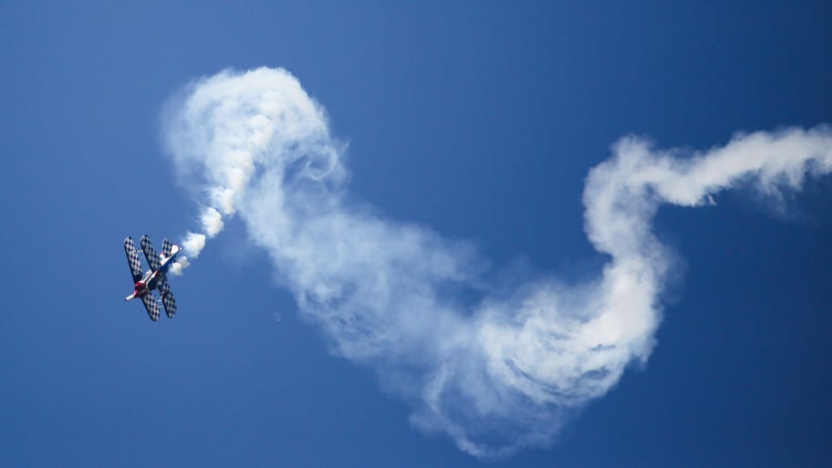 A Pitts S1S biplane aerobatic plane flies on the Swabian Alb, trailing white clouds of fog 