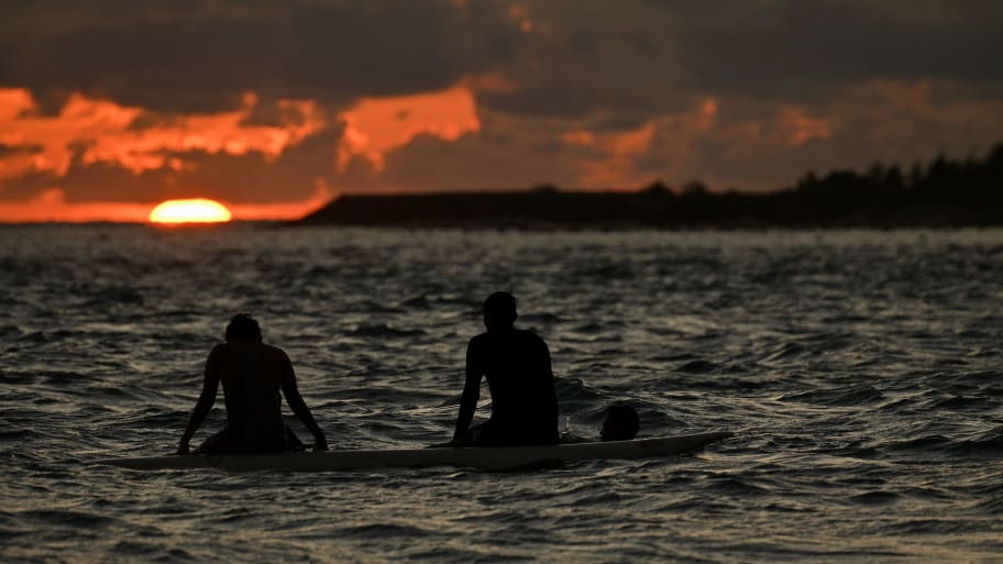 Boys surf during sunset in Lhoknga beach, Aceh province on May 27, 2023.