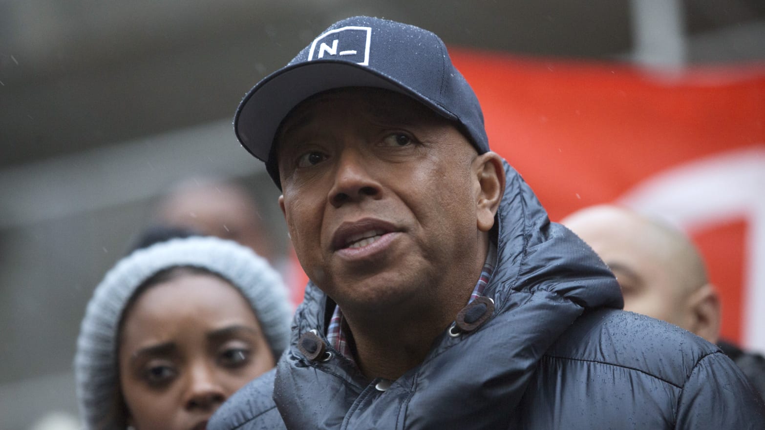 Russell Simmons, wearing a hat, prepares to speak at an outside event.