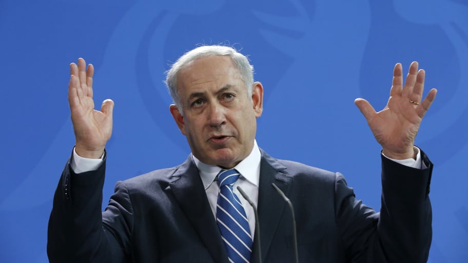 Benjamin Netanyahu speaks on stage with his hands raised.