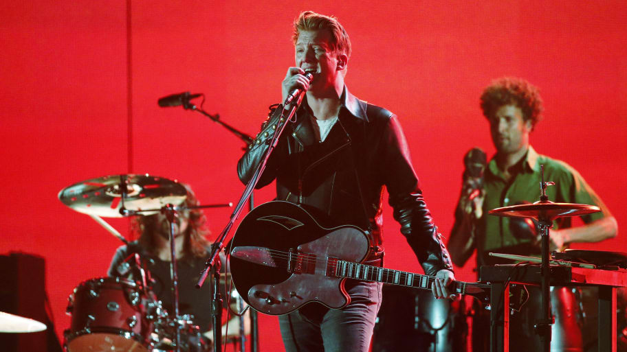 Josh Homme sings on stage alongside the Queens of Stone Age in front of a red background