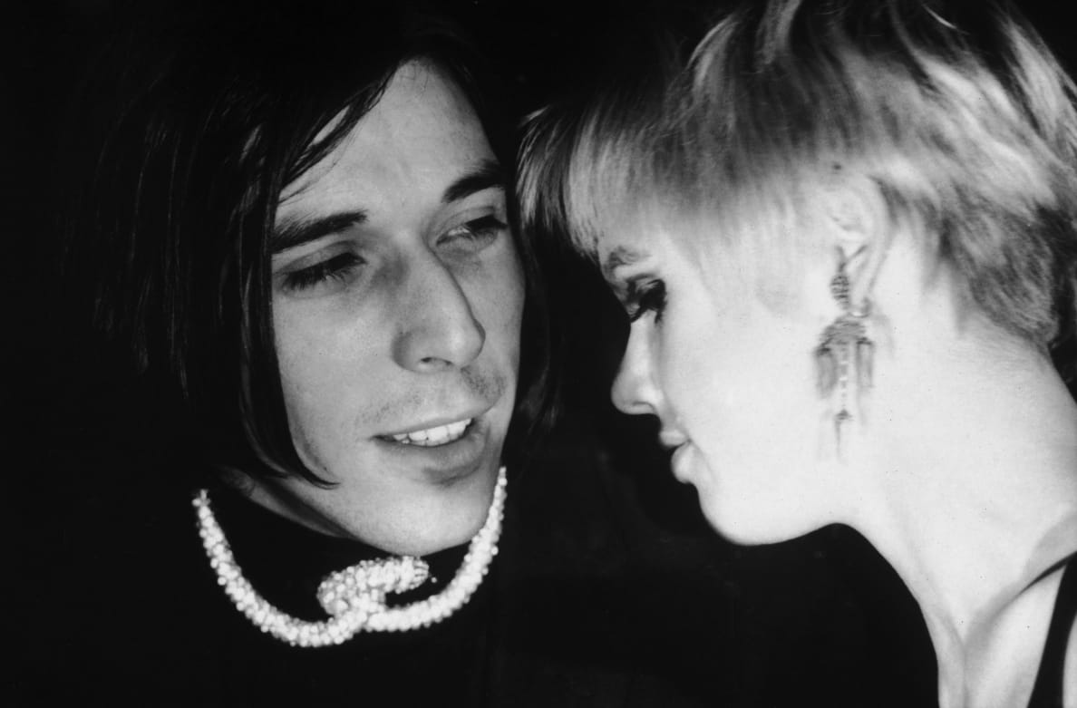 A black and white photo of The Velvet Underground’s John Cale and Edie Sedgwick talking to each other in 1966.