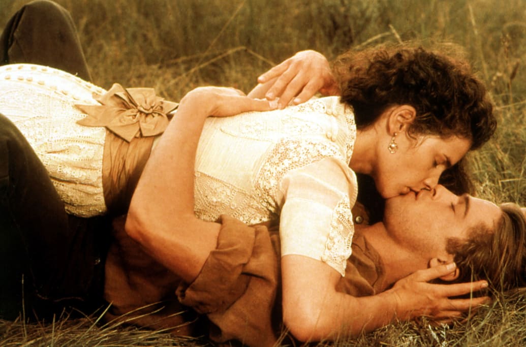 Julia Ormond and Brad Pitt laying in the grass and kissing in a still from 'Legends of the Fall'