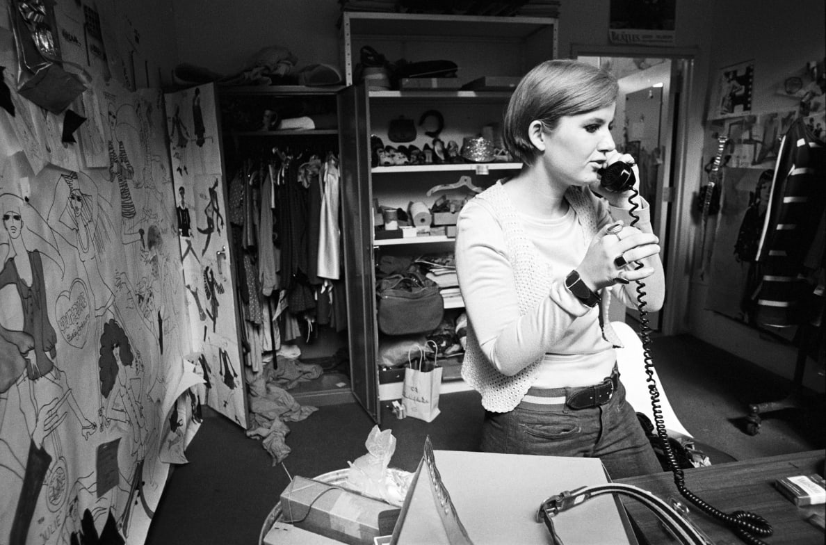 A black and white photo of fashion designer Betsey Johnson in 1966 on the phone in her studio