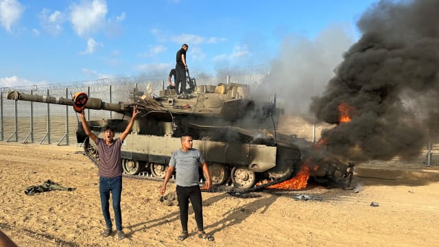 Palestinians cheer as an Israeli military vehicle burns after it was hit by Palestinian gunmen