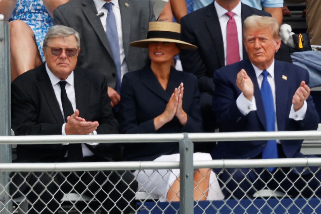 Donald Trump sits next to his wife, Melania, and her father on bleachers