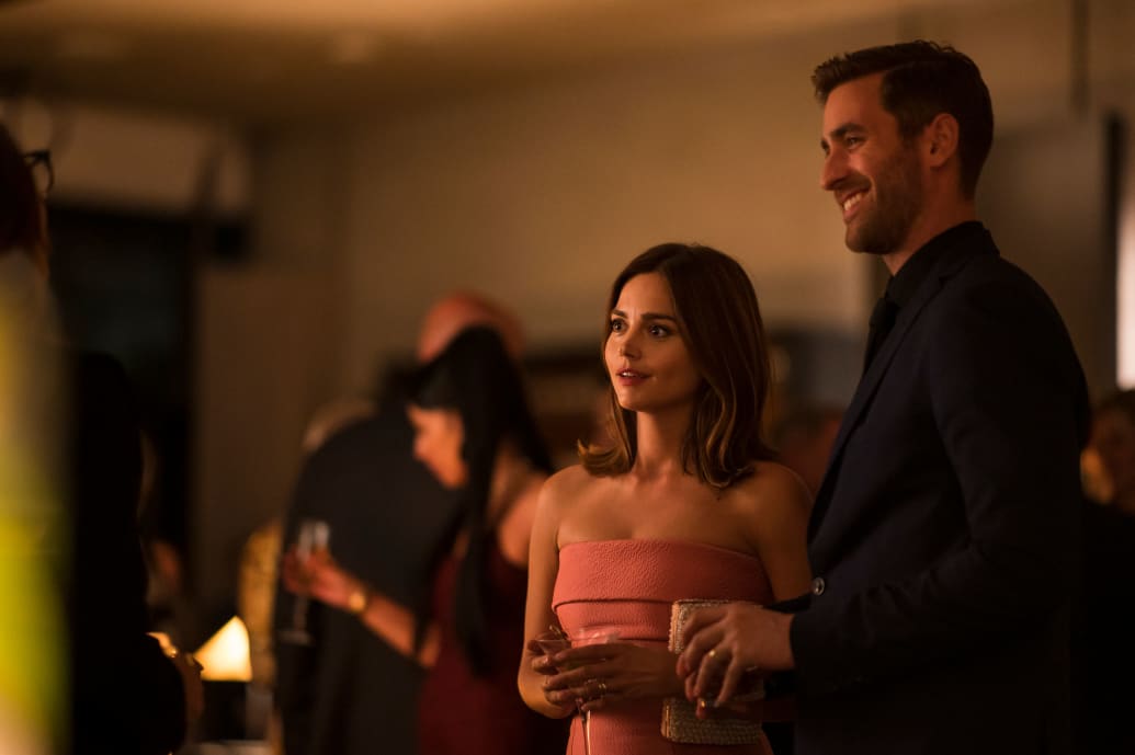  ]Oliver Jackson-Cohen and Jenna Coleman stand next to each other in a dark room in a still from ‘Wilderness’