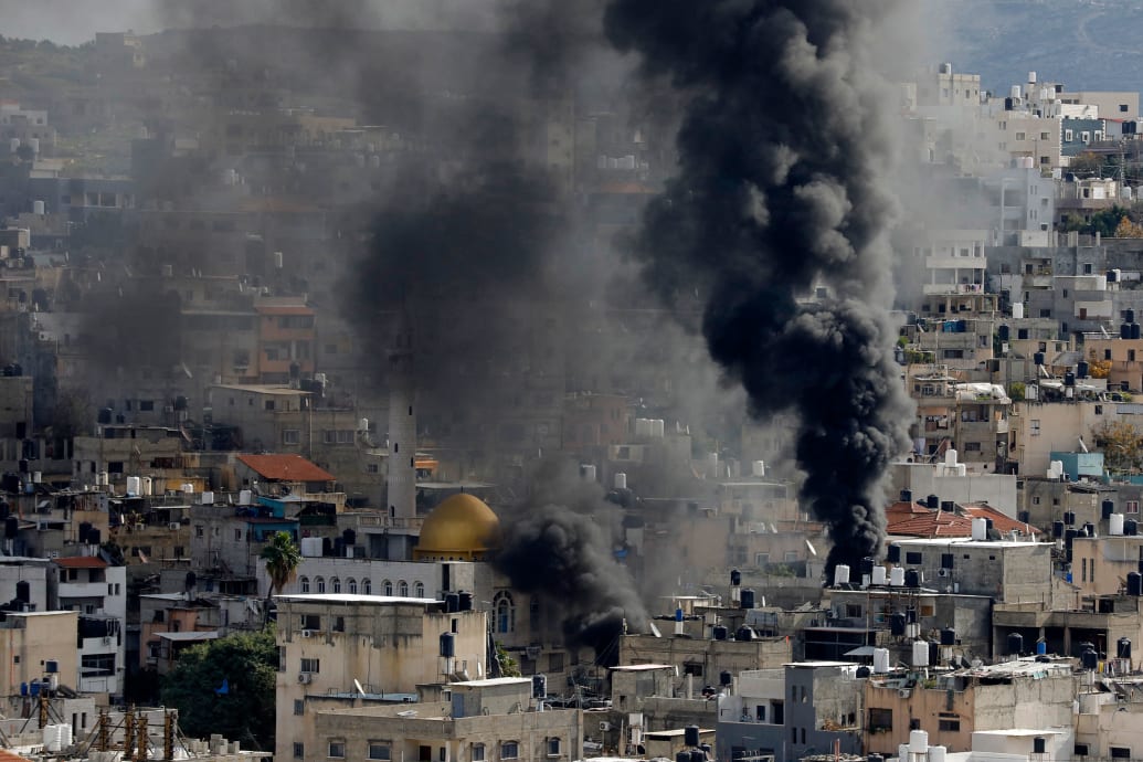 An aerial view of bombed out buildings with smoke rising near a Palestinian refugee camp
