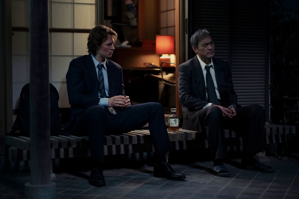 Ken Watanabe and Ansel Elgort sit on a stoop in a still from ‘Tokyo Vice’