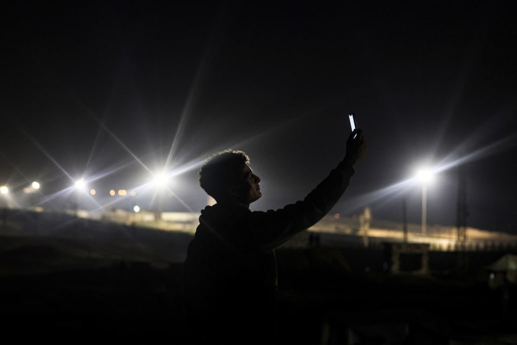 A photo of a Palestinian at the Egyptian border holds his phone up looking for a signal