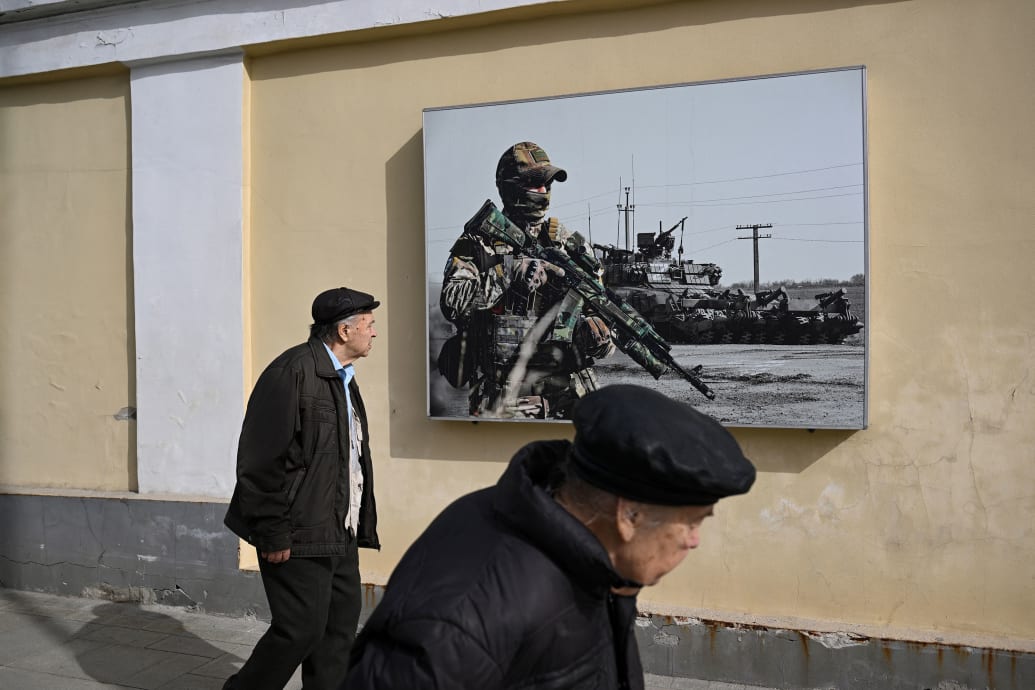A photo of pedestrians walking past a poster of Russian soldiers in Moscow