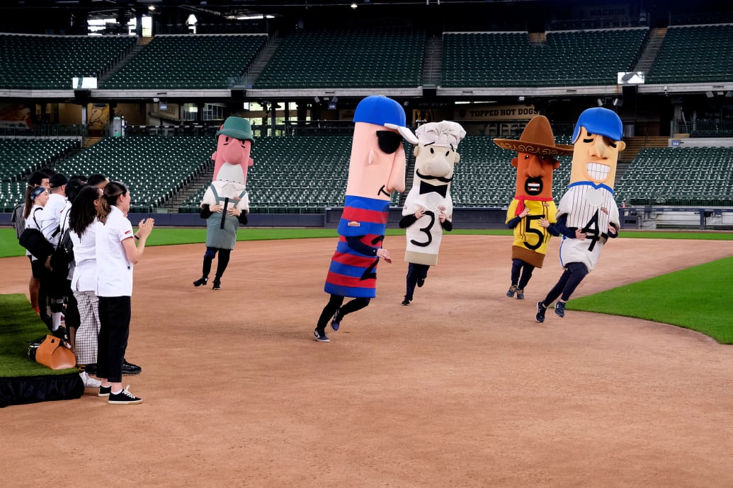 The contestants of Top Chef watch as characters run around a baseball field. 