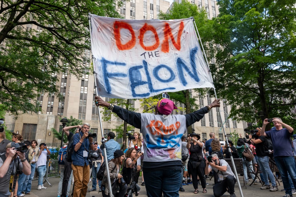 A person holds a sign that says "Don the Felon"