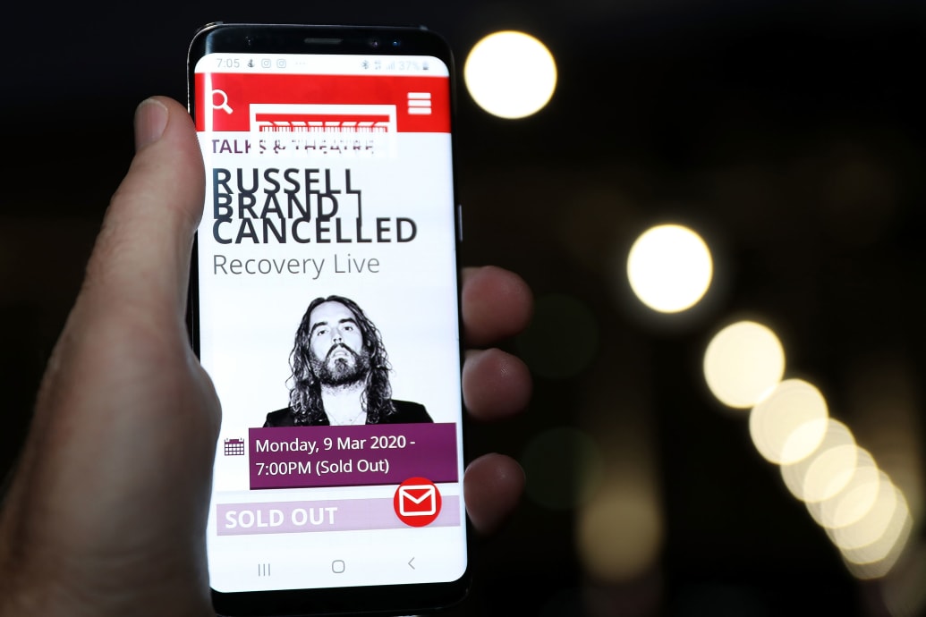 A phone shows an ad for Russell Brand's show that has been cancelled