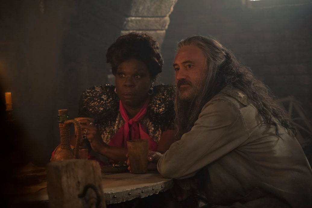 Leslie Jones and Taika Waititi sit at a table in a still from a movie 