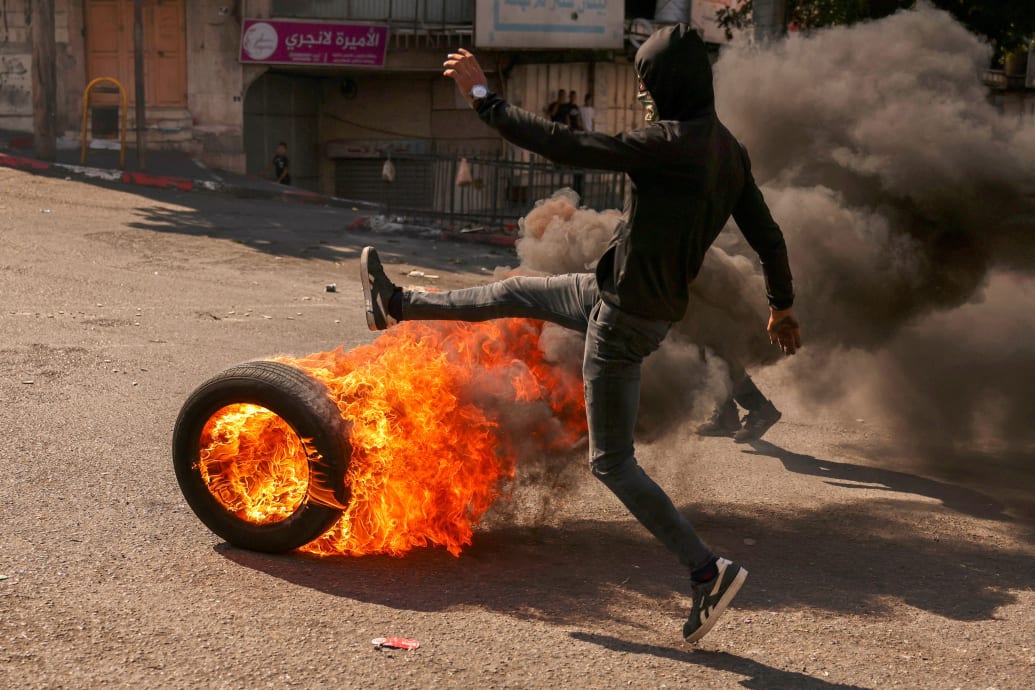A Palestinian demonstrator kicks a flaming tyre towards Iraeli security forces