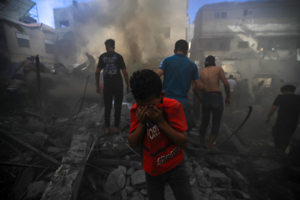 A small boy covers his face as civilians search through rubble behind him in Gaza