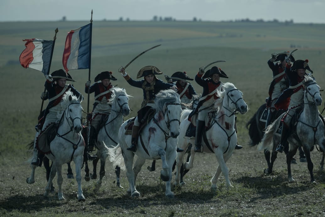A band of soldiers on horses led by Joaquin Phoenix in a still from "Napoleon,"