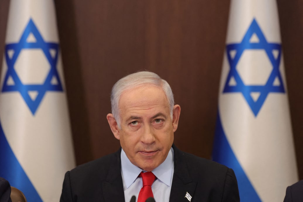 Benjamin Netanyahu sits between two Israeli flags