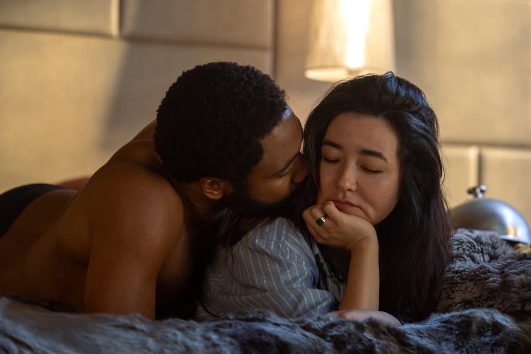Maya Erskine and Donald Glover lay in bed together in a still from ‘Mr. and Mrs. Smith’